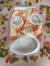 Load image into Gallery viewer, Close-up of a fabric item with an all-over novelty print featuring frosted toaster pastries with rainbow sprinkles and crimped orange edges, on a pink background
