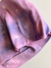 Load image into Gallery viewer, Close-up of a fabric item with an all-over galaxy-style print featuring a color-wash design in pink and purple with white speckles resembling stars

